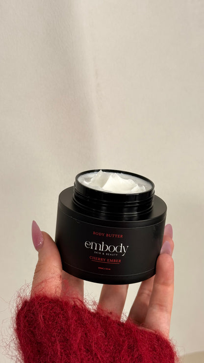 Hand holding a black jar of 'Embody' body butter against a neutral background